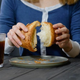 Hands tearing croissant in half beside cup of coffee